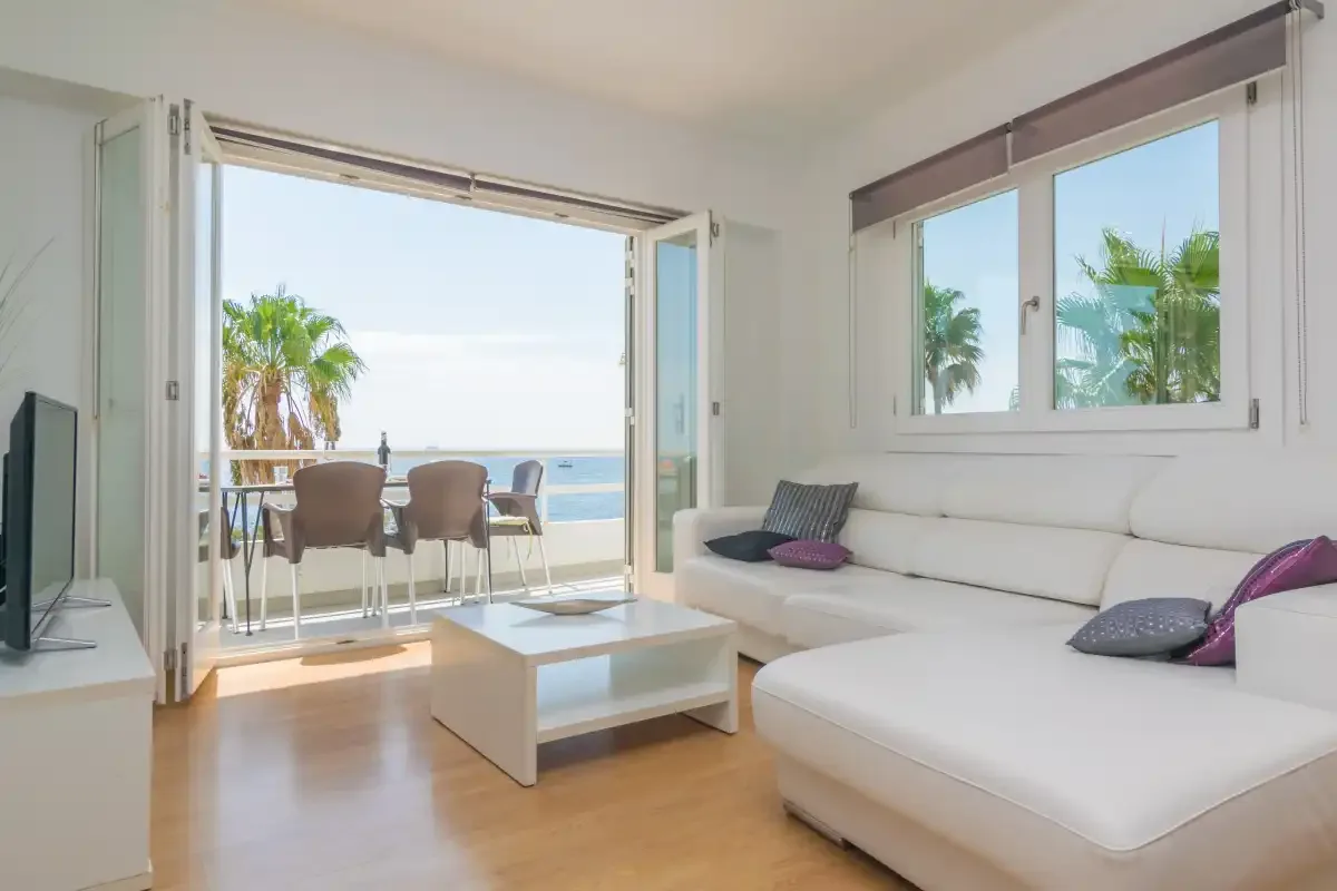 A bright living room opens onto a balcony with a view of the sea.