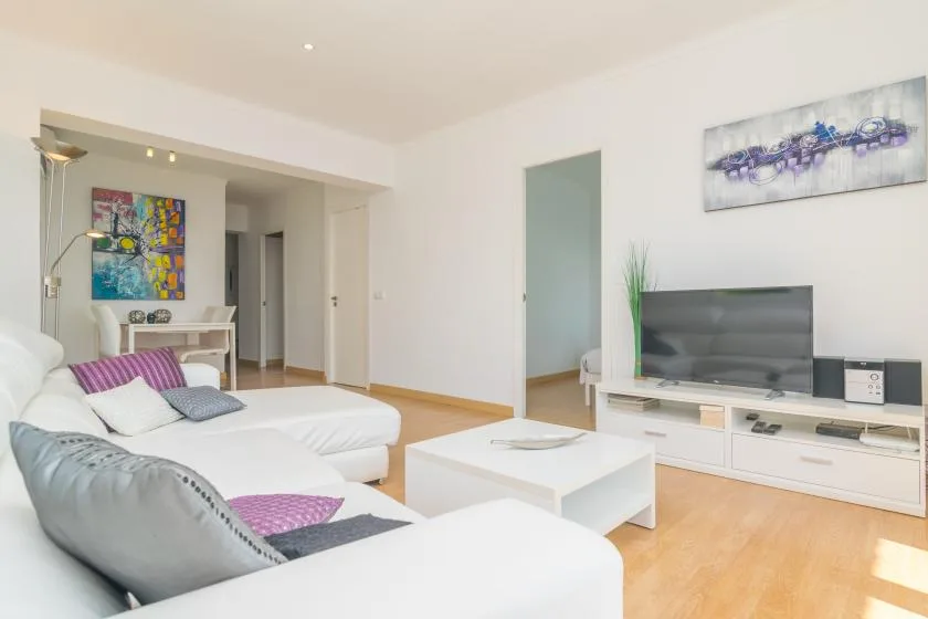A bright living room with white seating, a coffee table, and a television.