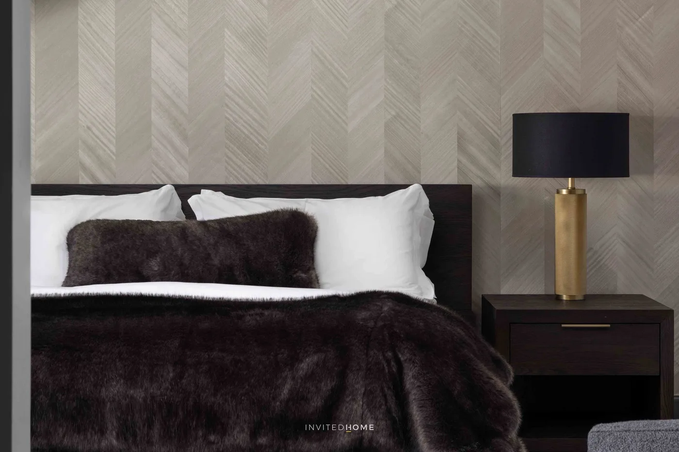Un dormitorio con una cama oscura, almohadas blancas y una lámpara de noche.