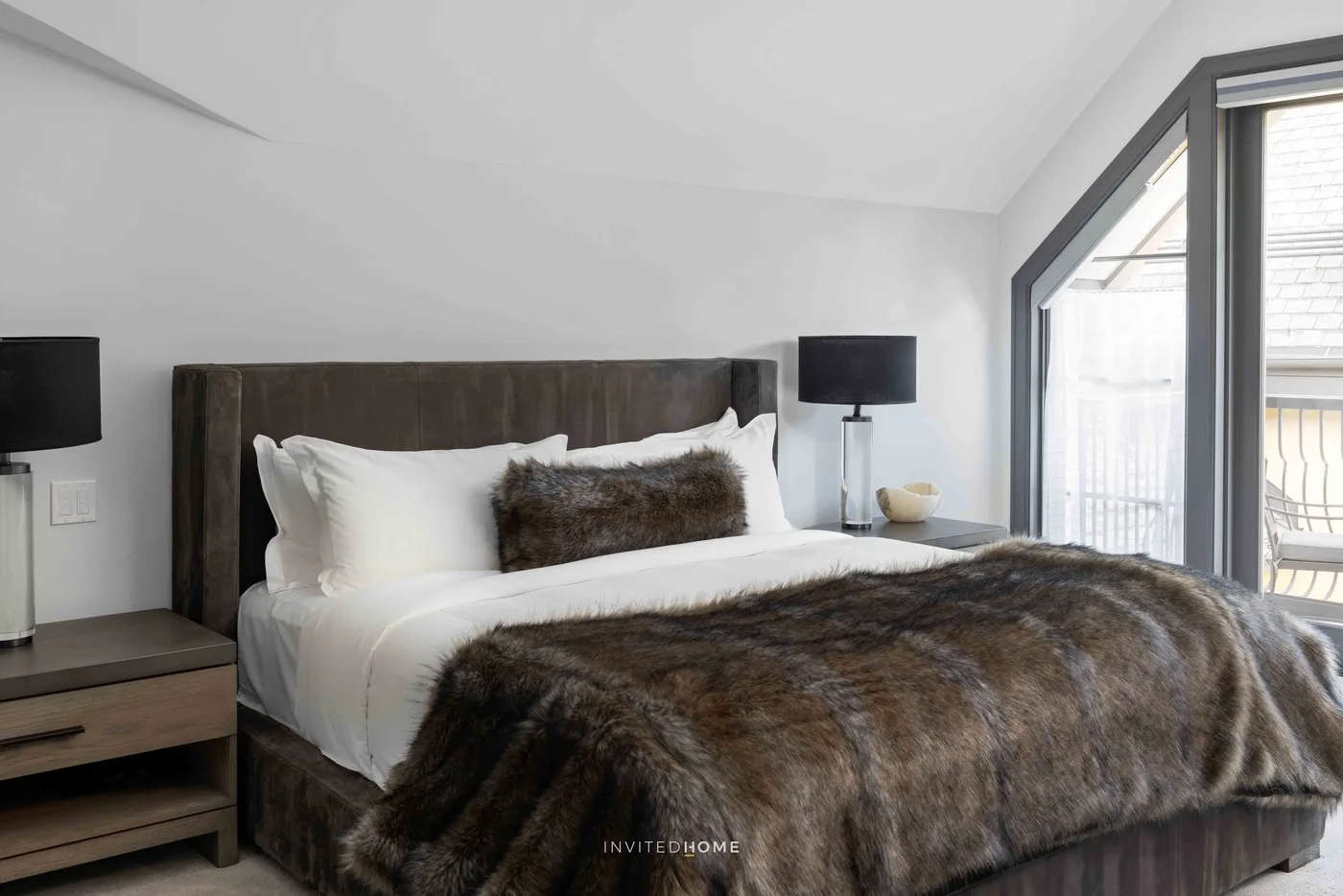 Un dormitorio con una cama vestida con ropa blanca y una manta oscura de pelo.