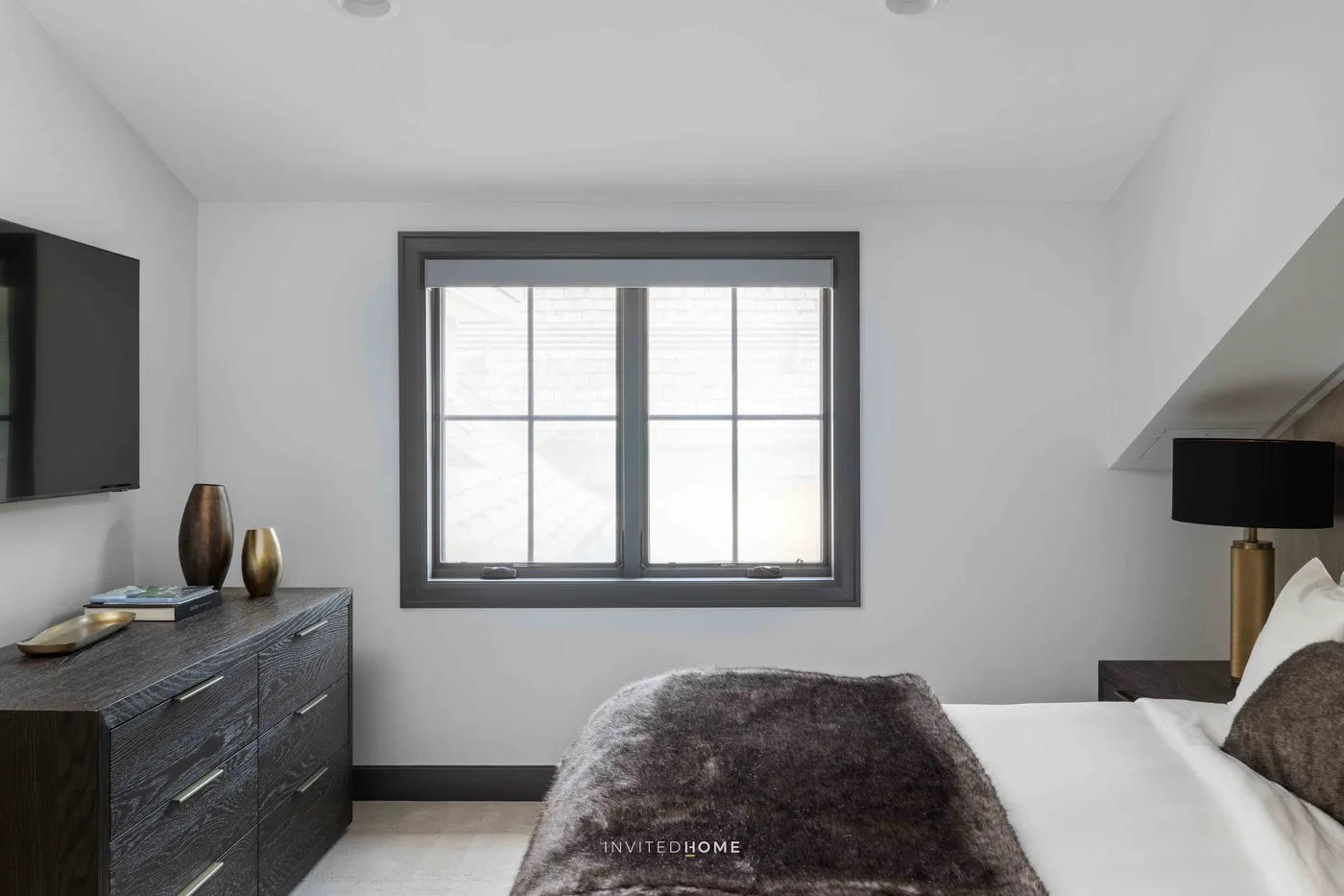 Un dormitorio con una cama, una cómoda oscura y una ventana grande.