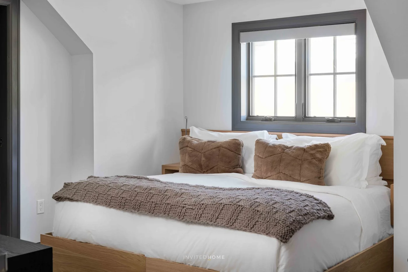 Un dormitorio luminoso con una cama tendida y una ventana detrás.