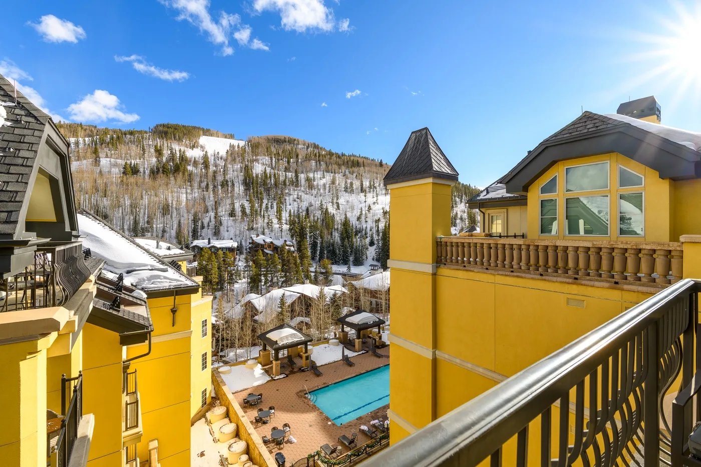 Un edificio amarillo da a una piscina exterior y una ladera de montaña nevada.