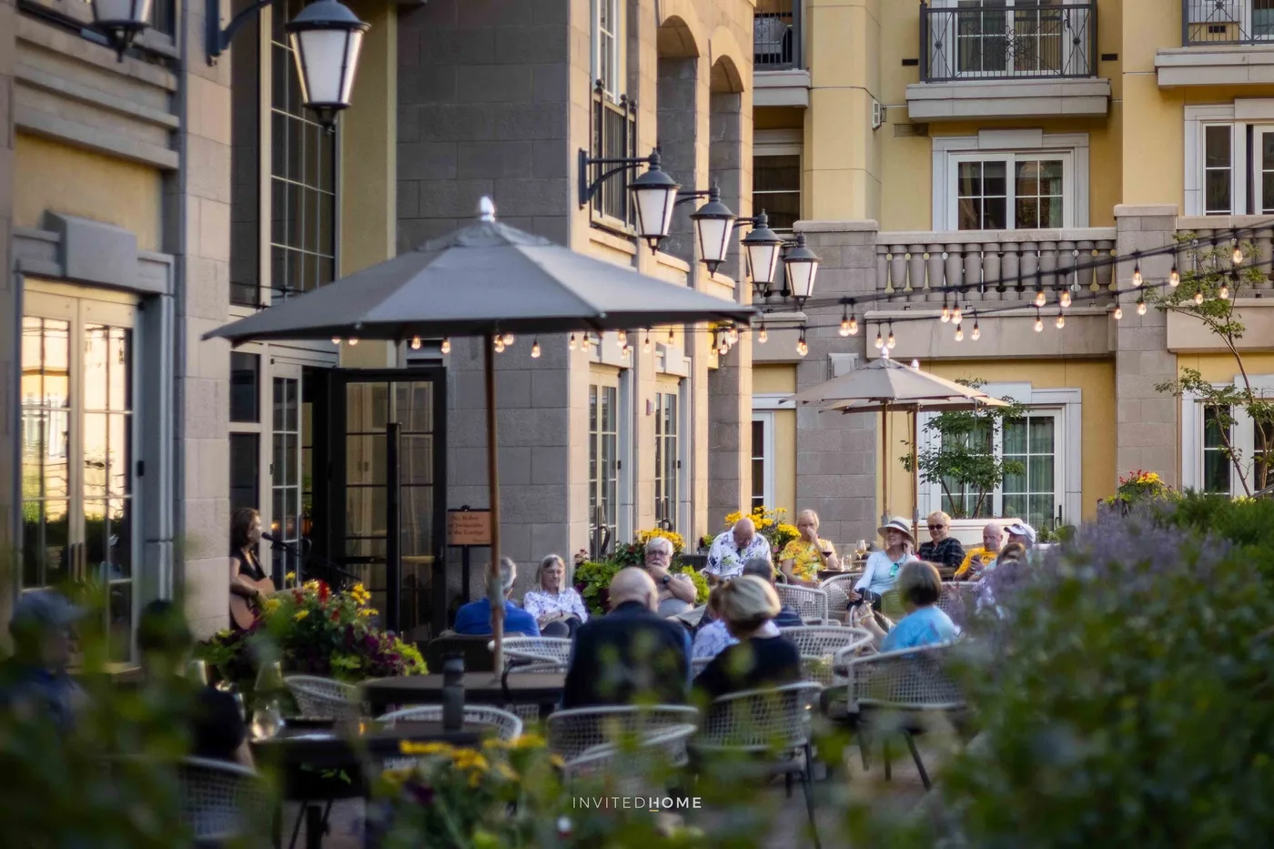 Un comedor al aire libre en un patio tiene mesas, sombrillas y luces colgantes.