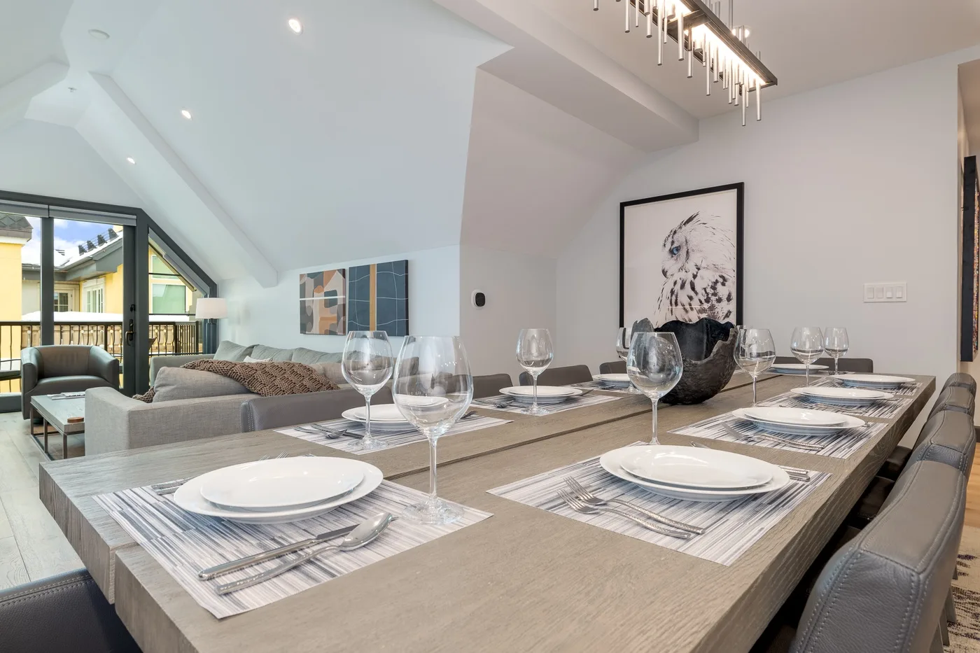 Comedor con una mesa larga preparada con platos y copas junto a una zona de estar.