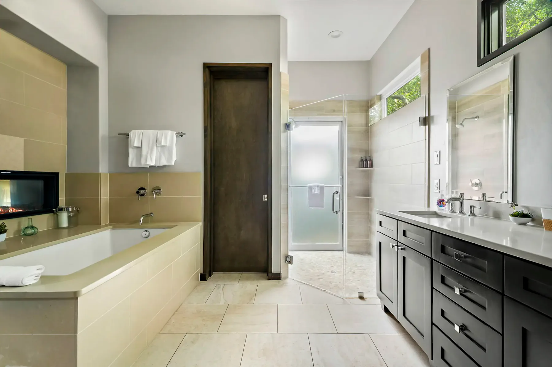 Baño moderno con una bañera, una ducha con cerramiento de vidrio y un mueble de lavabo doble. Tonos neutros y una toalla colgada junto a la bañera.
