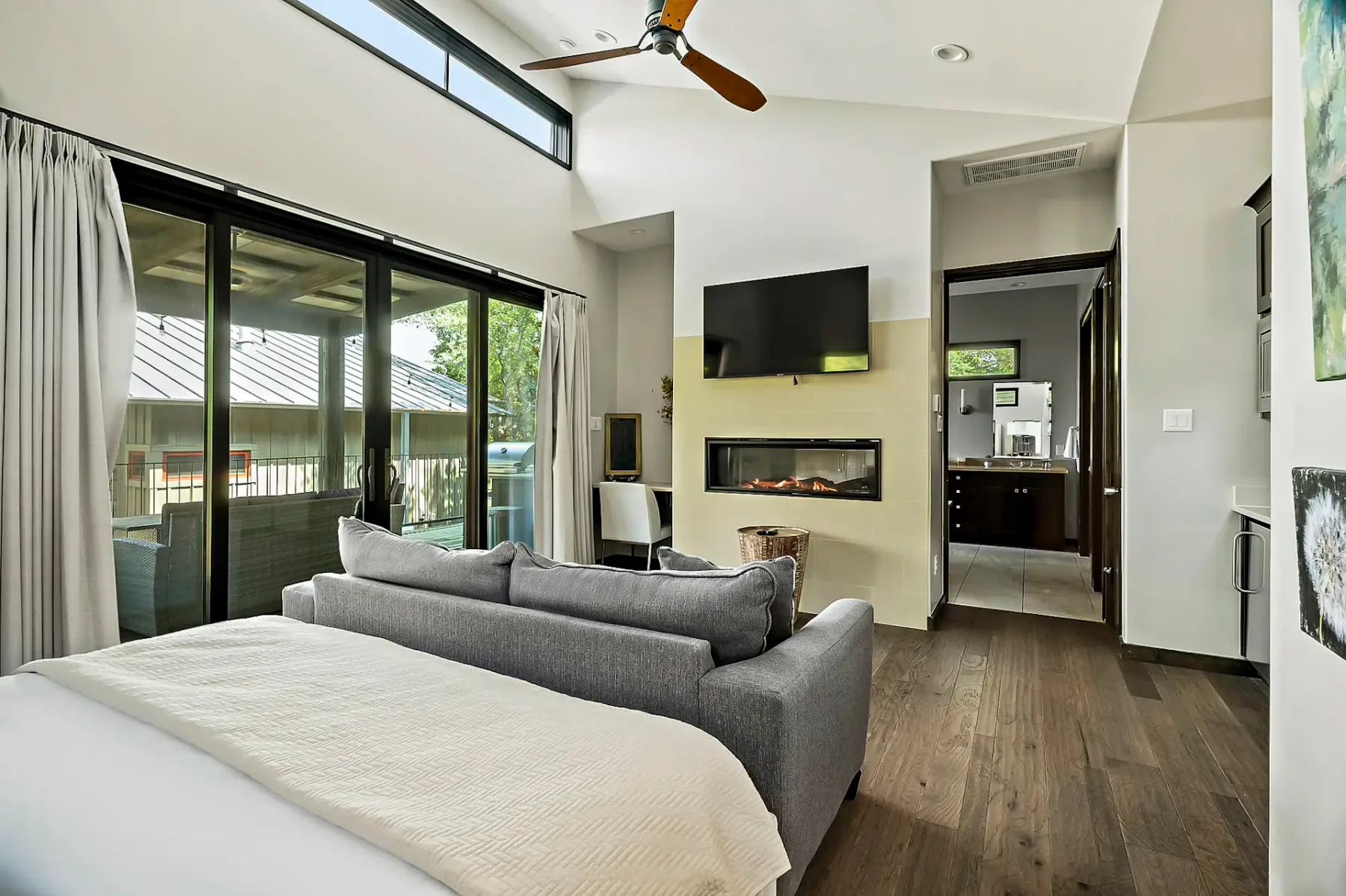 A bedroom with a bed, seating, and a wall-mounted television facing glass doors.