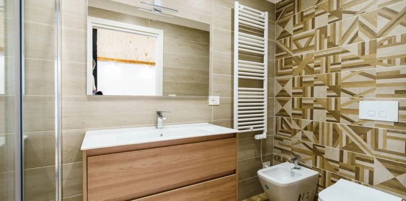 A bathroom with a vanity sink, wall-mounted towel warmer, and patterned tile.