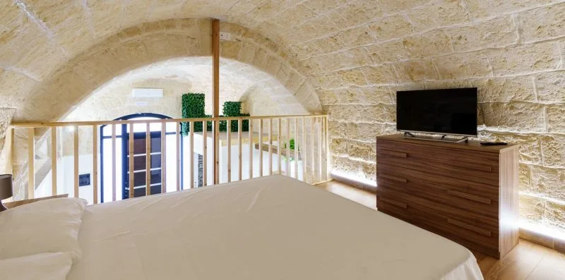 A bedroom with a bed, wooden dresser, and television beneath a stone arch.