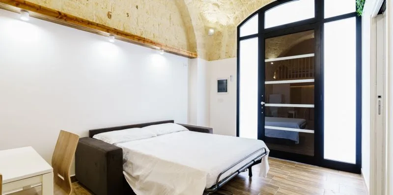 A bedroom with a bed beside a tall black-framed glass door.