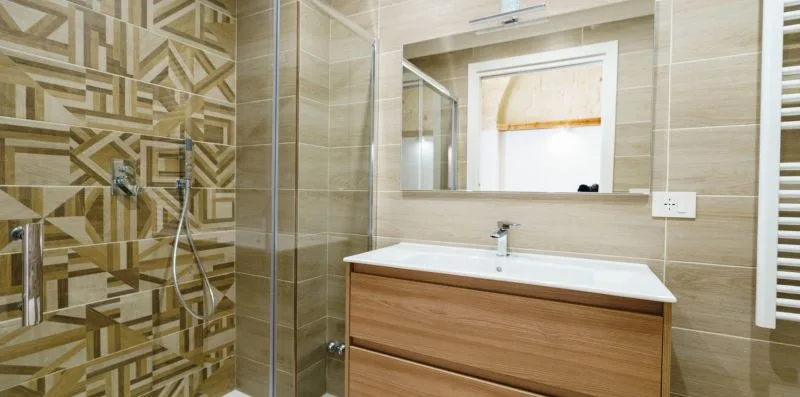 A bathroom vanity with a sink sits beside a glass shower and patterned tile.