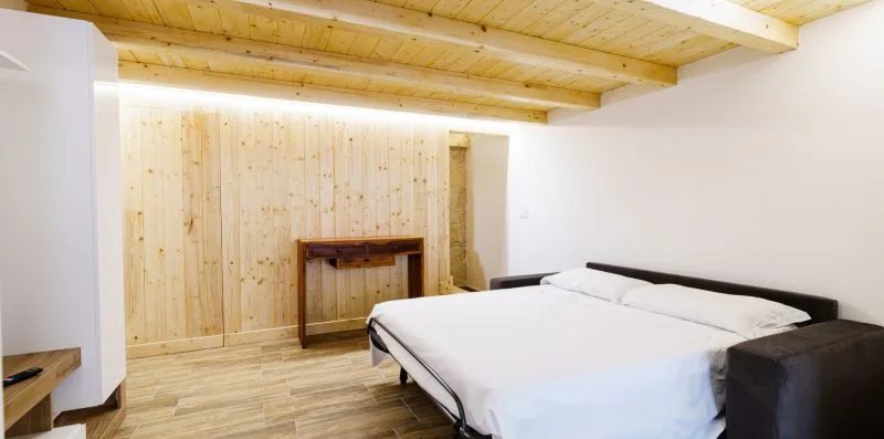 A bedroom with a large bed and light wood ceiling beams.