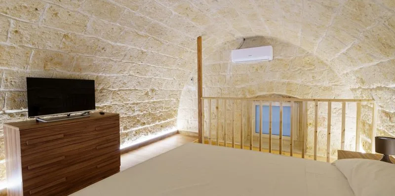 A bedroom beneath a stone vaulted ceiling has a bed, television, and wooden railing.