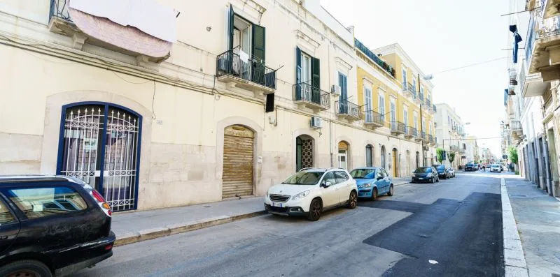 A narrow urban street lined with multi-story buildings and parked cars.