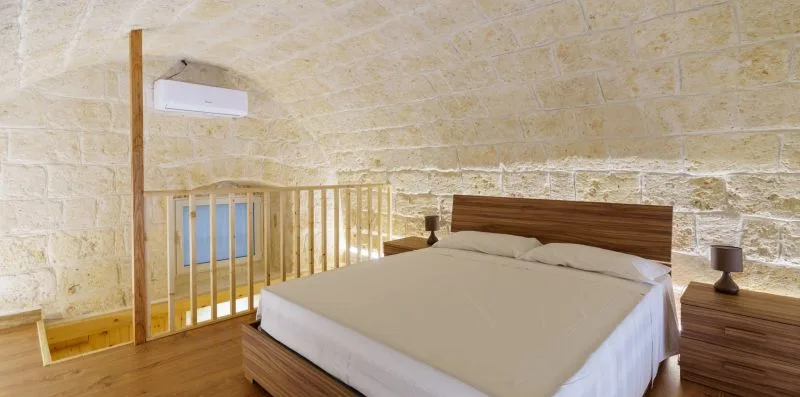 A bedroom with a bed, wooden headboard, and pale stone walls.