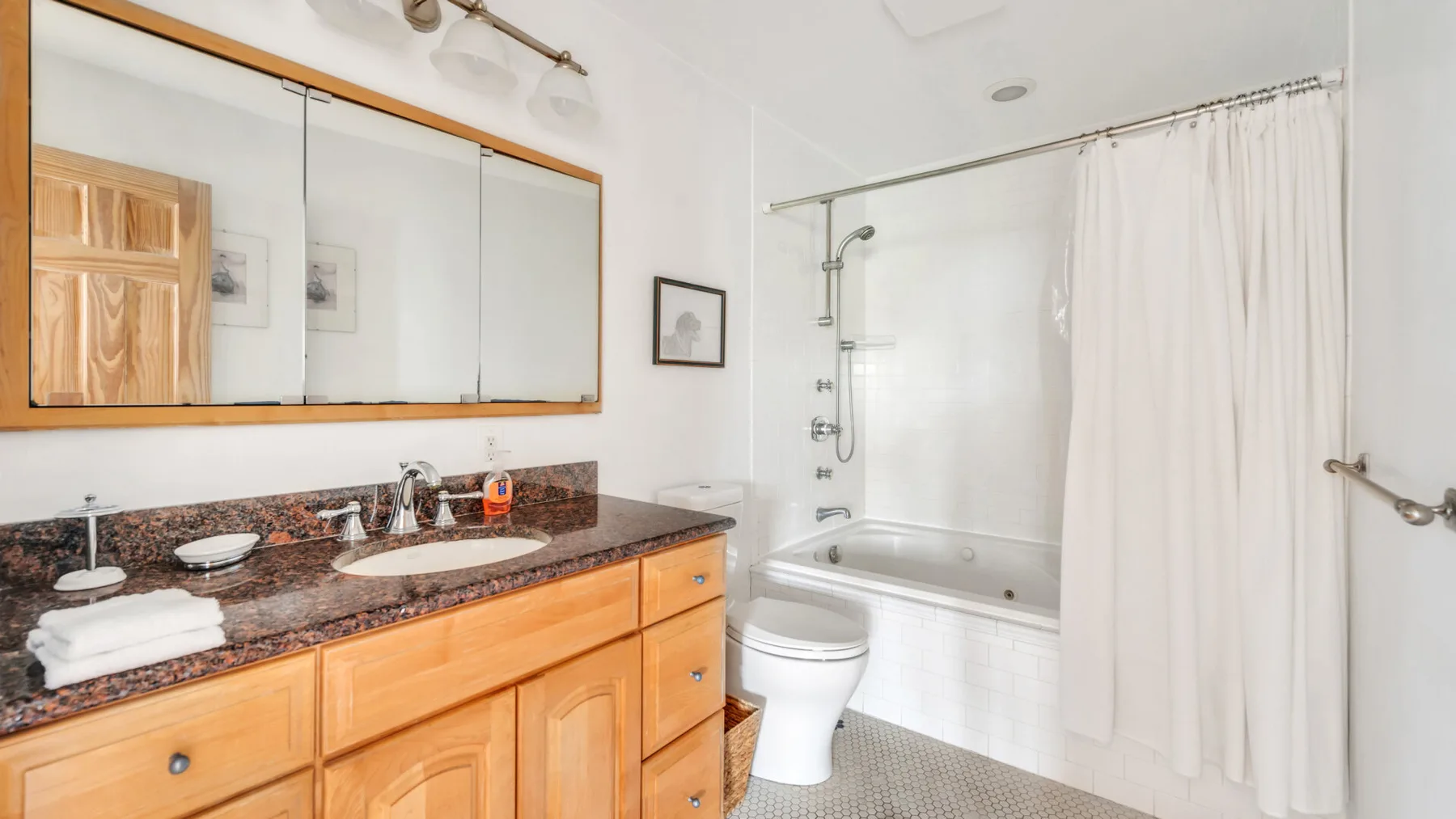 Un baño con un largo tocador, lavabo, inodoro y bañera con cortina de ducha.