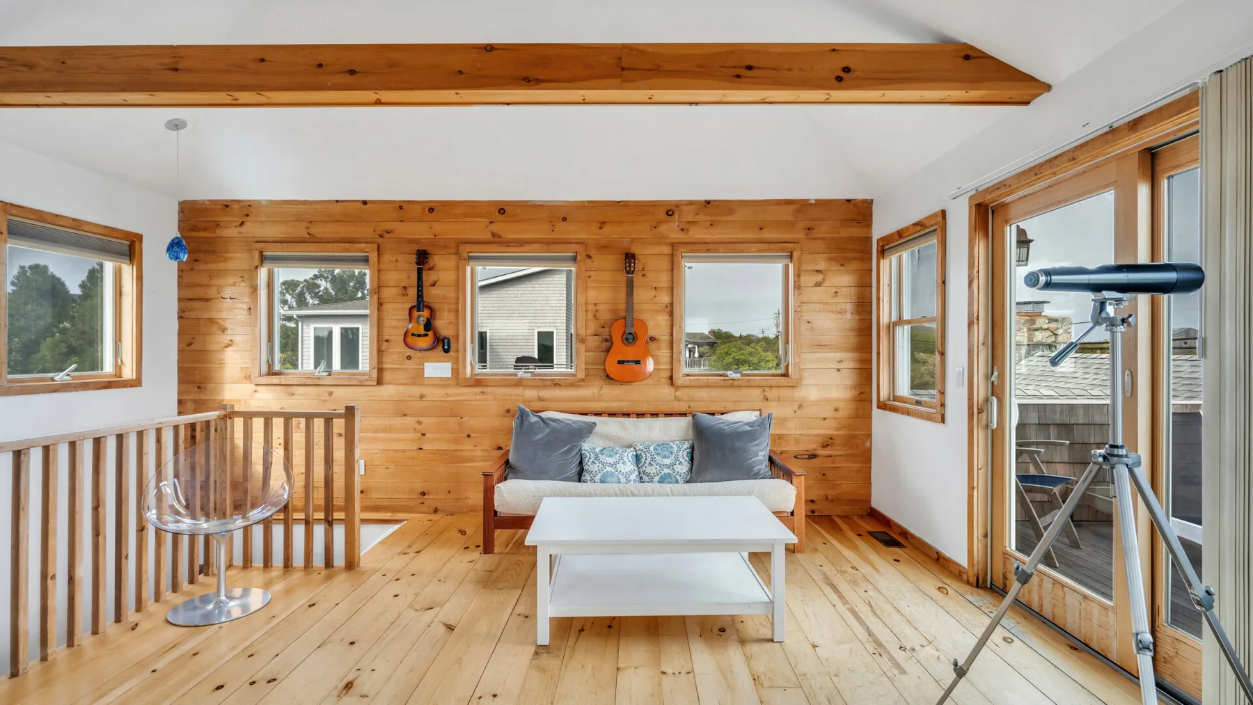 Una sala revestida de madera con sofá, mesa de centro y telescopio junto a las ventanas.