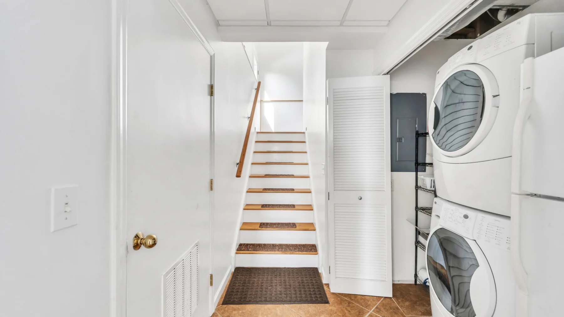 Un cuarto de lavandería estrecho con lavadora y secadora apiladas junto a una escalera.