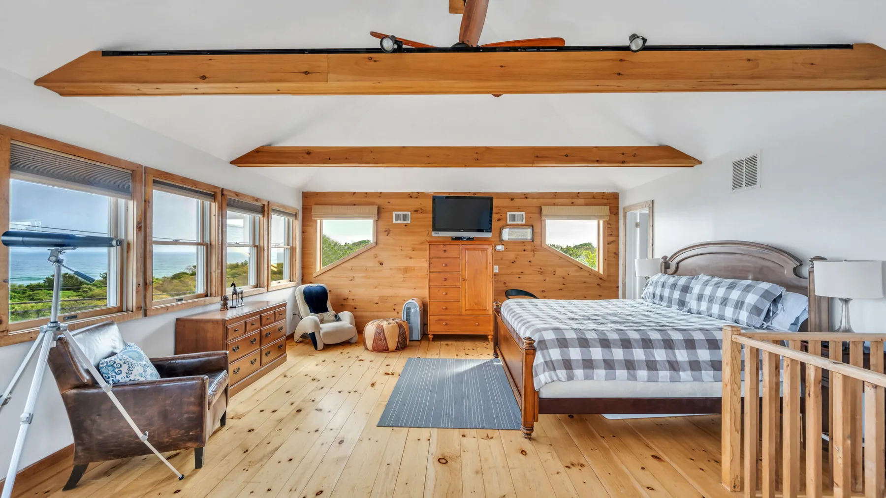 Un dormitorio revestido de madera, con una cama y grandes ventanas que dan a zonas verdes.