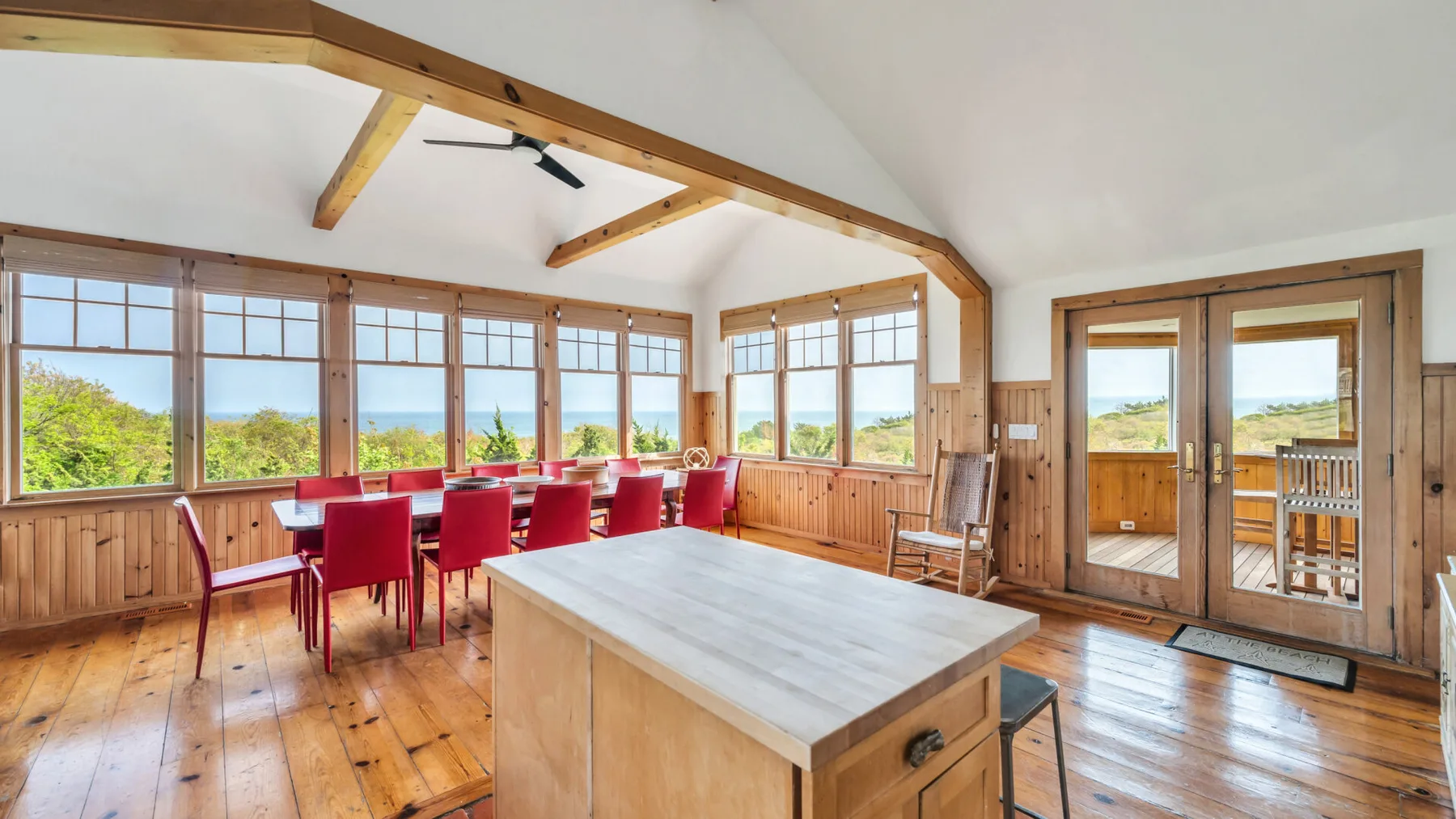 Un comedor luminoso con una mesa larga, grandes ventanas y vigas de madera.