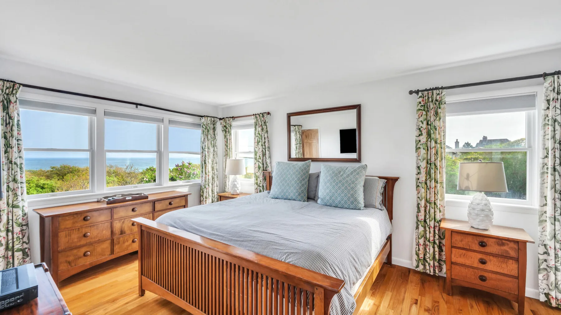 Un dormitorio luminoso con una cama grande, muebles de madera y amplias ventanas.