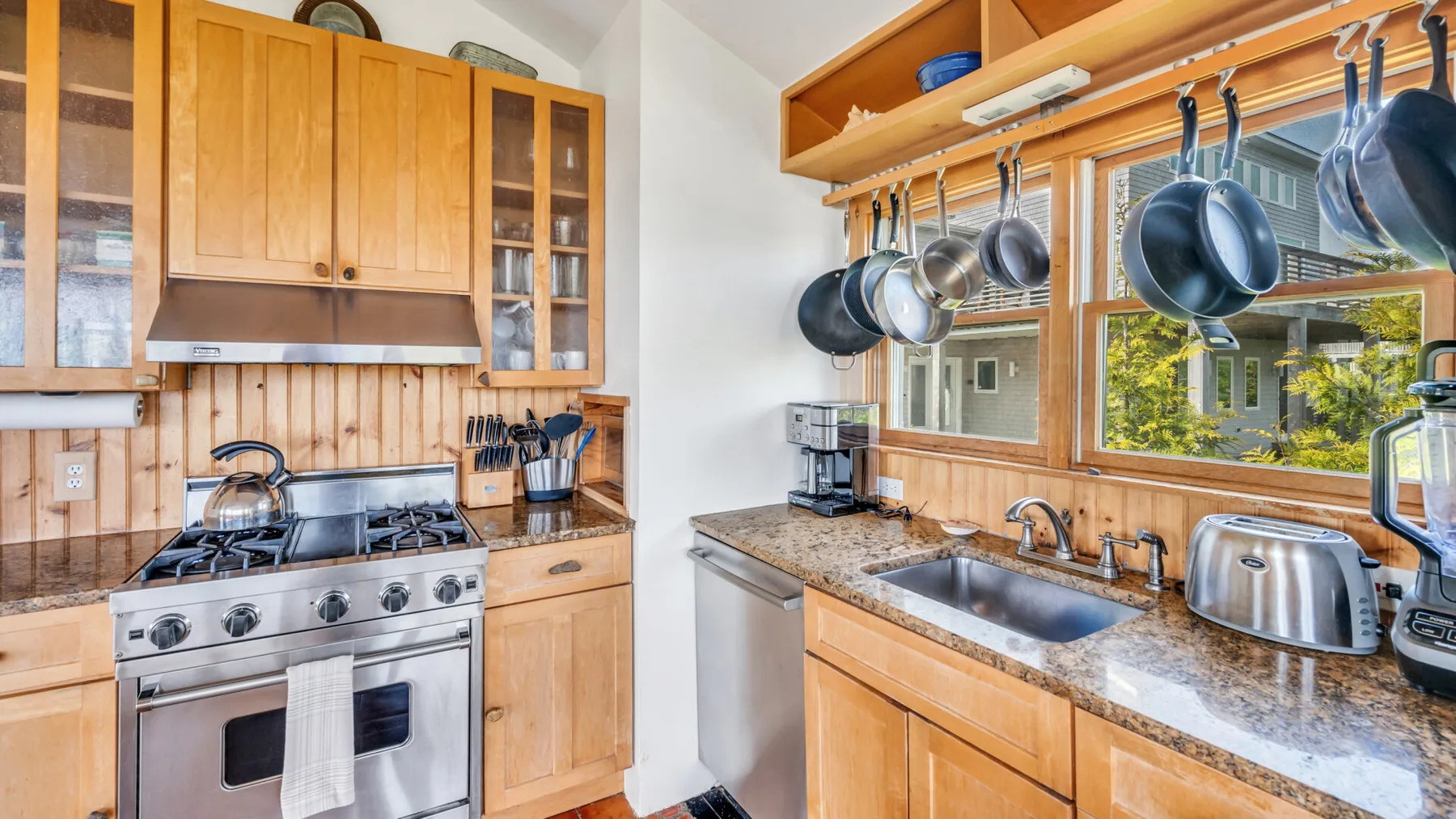 Una cocina con gabinetes de madera, una estufa y un fregadero bajo una ventana.