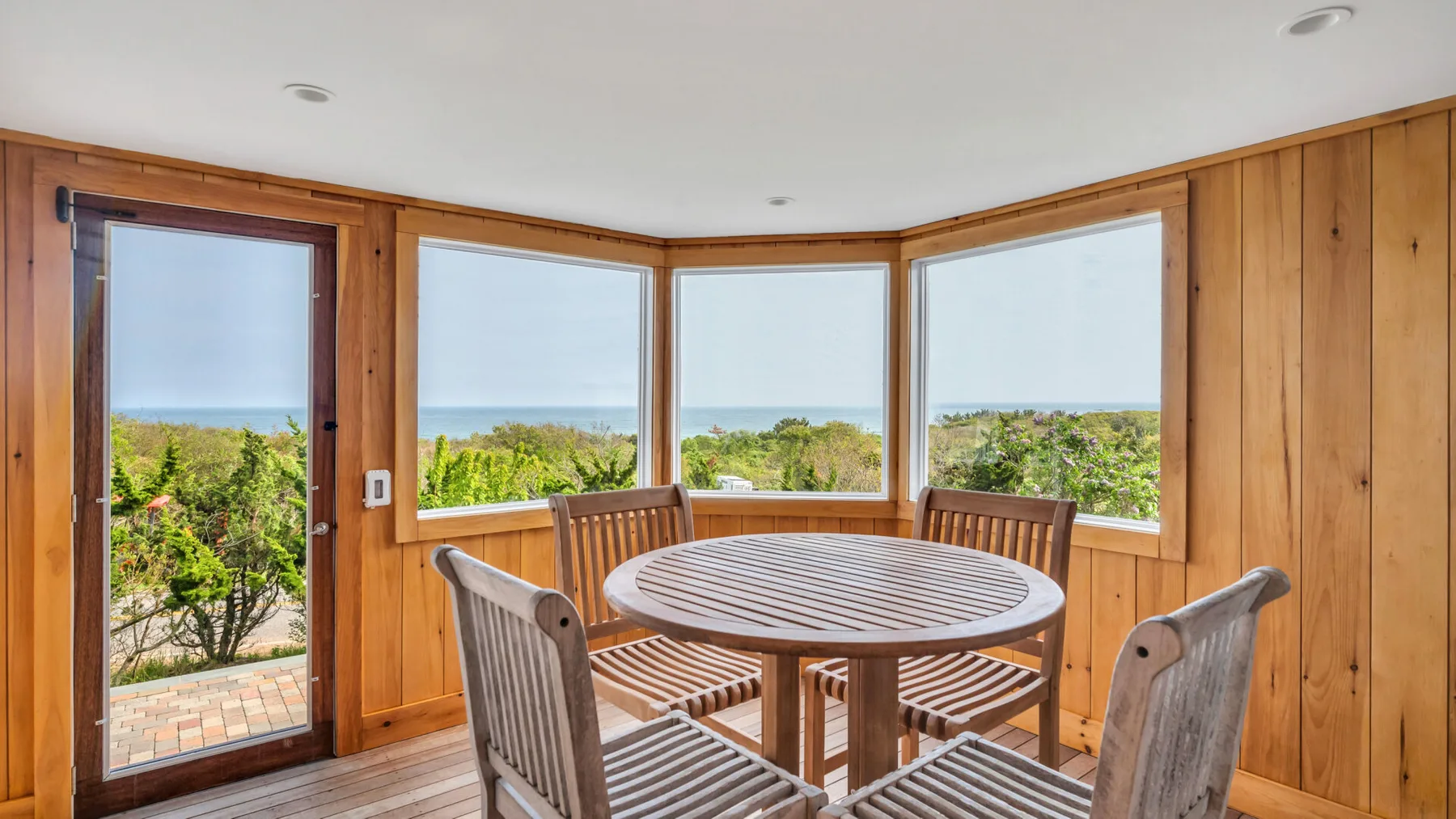 Un solárium revestido de madera tiene una mesa ovalada y asientos junto a grandes ventanas.