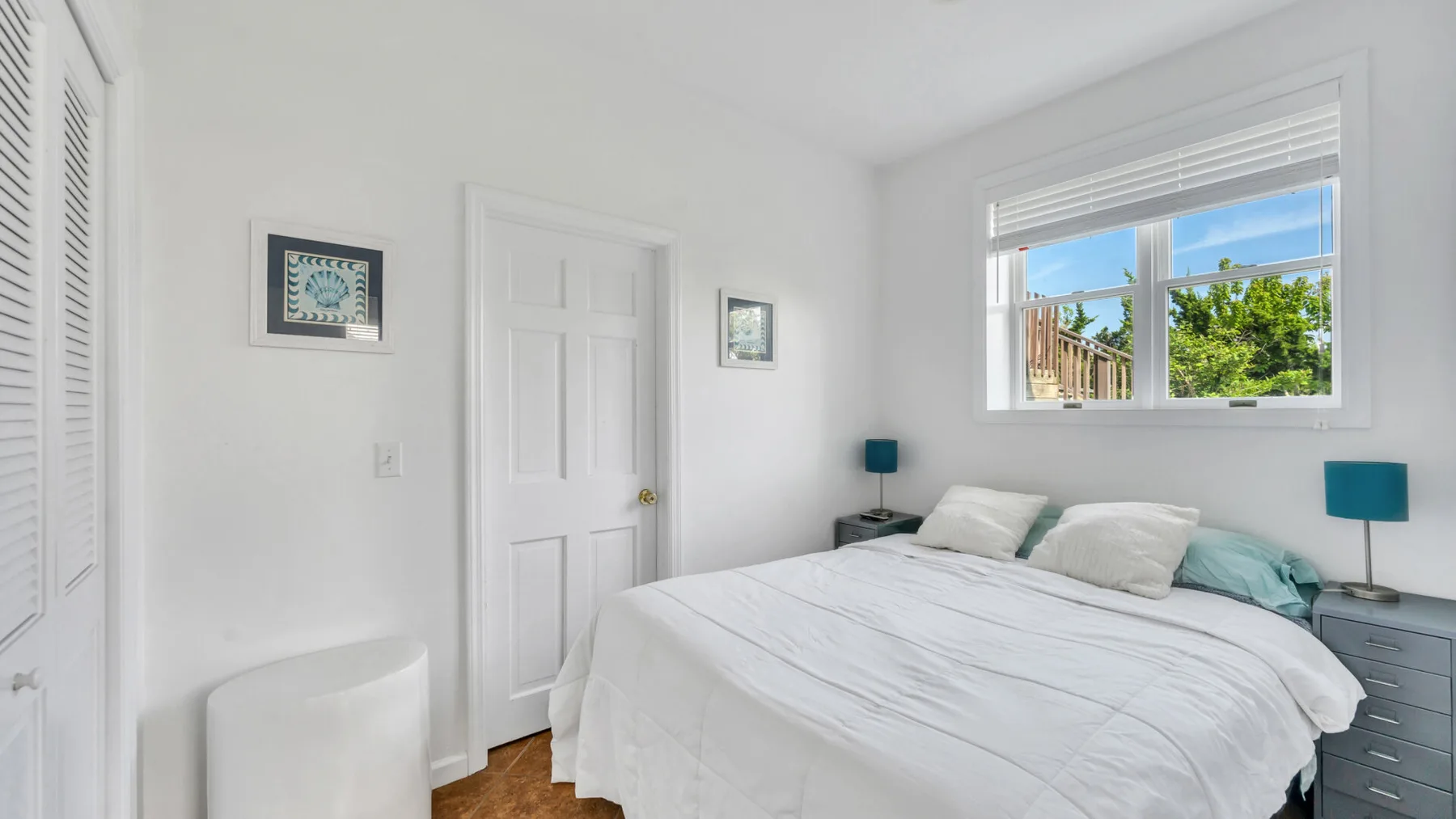Un dormitorio luminoso tiene una cama bajo una ventana con vistas a la vegetación.