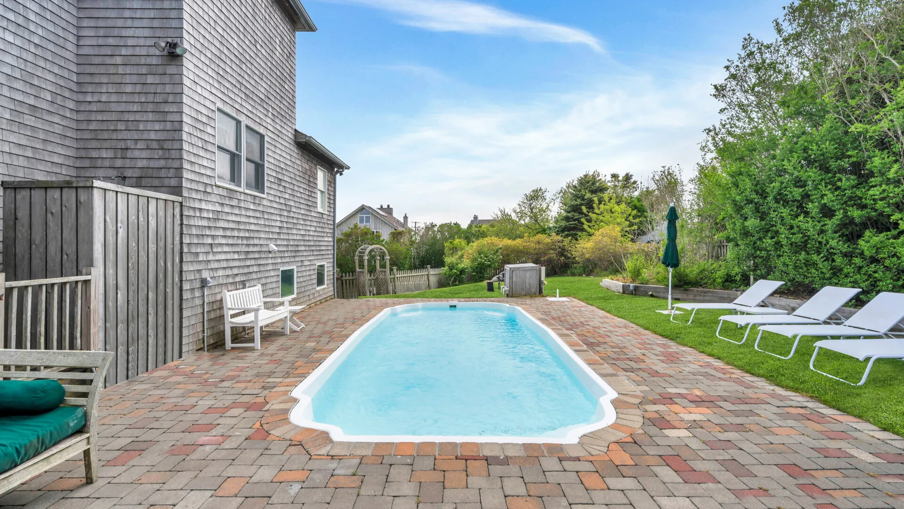 Una piscina al aire libre está rodeada por un patio pavimentado y césped.