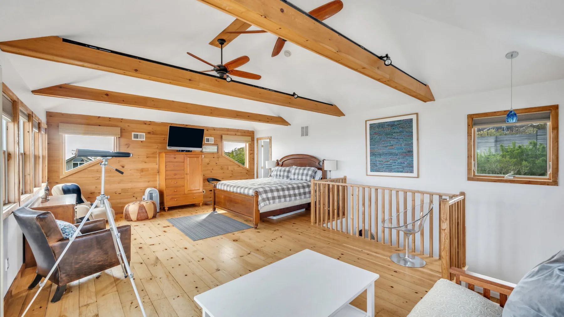 Un dormitorio tipo loft luminoso con una cama, vigas de madera y una barandilla.