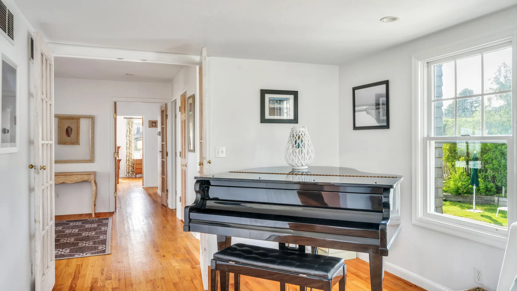Un pasillo luminoso da a una habitación con un piano junto a una ventana grande.
