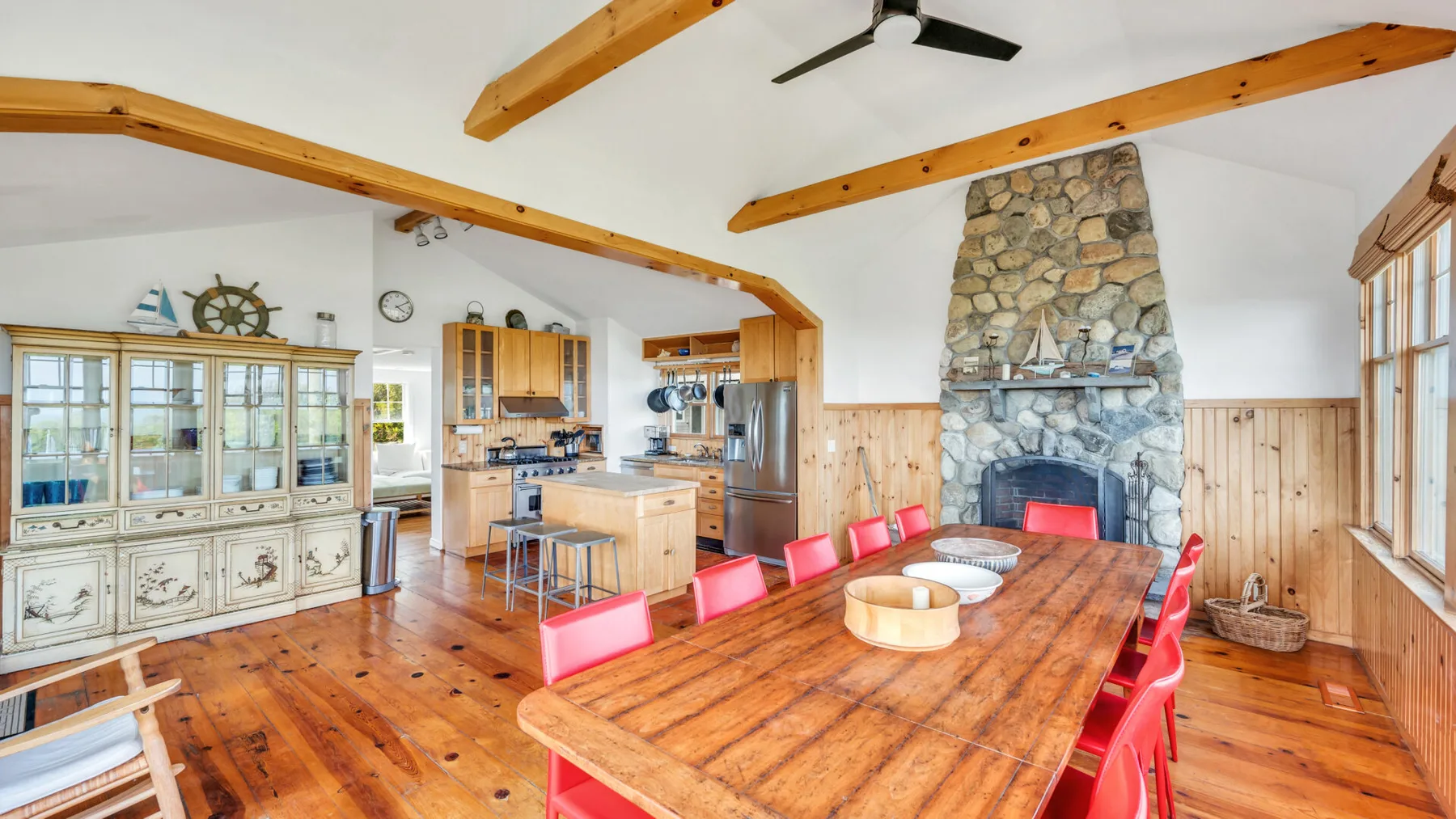 Un comedor con una larga mesa de madera y asientos rojos junto a una chimenea de piedra.