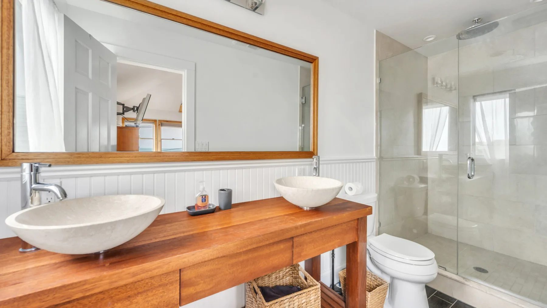 Un baño con un tocador de madera, dos lavabos y una ducha de vidrio.