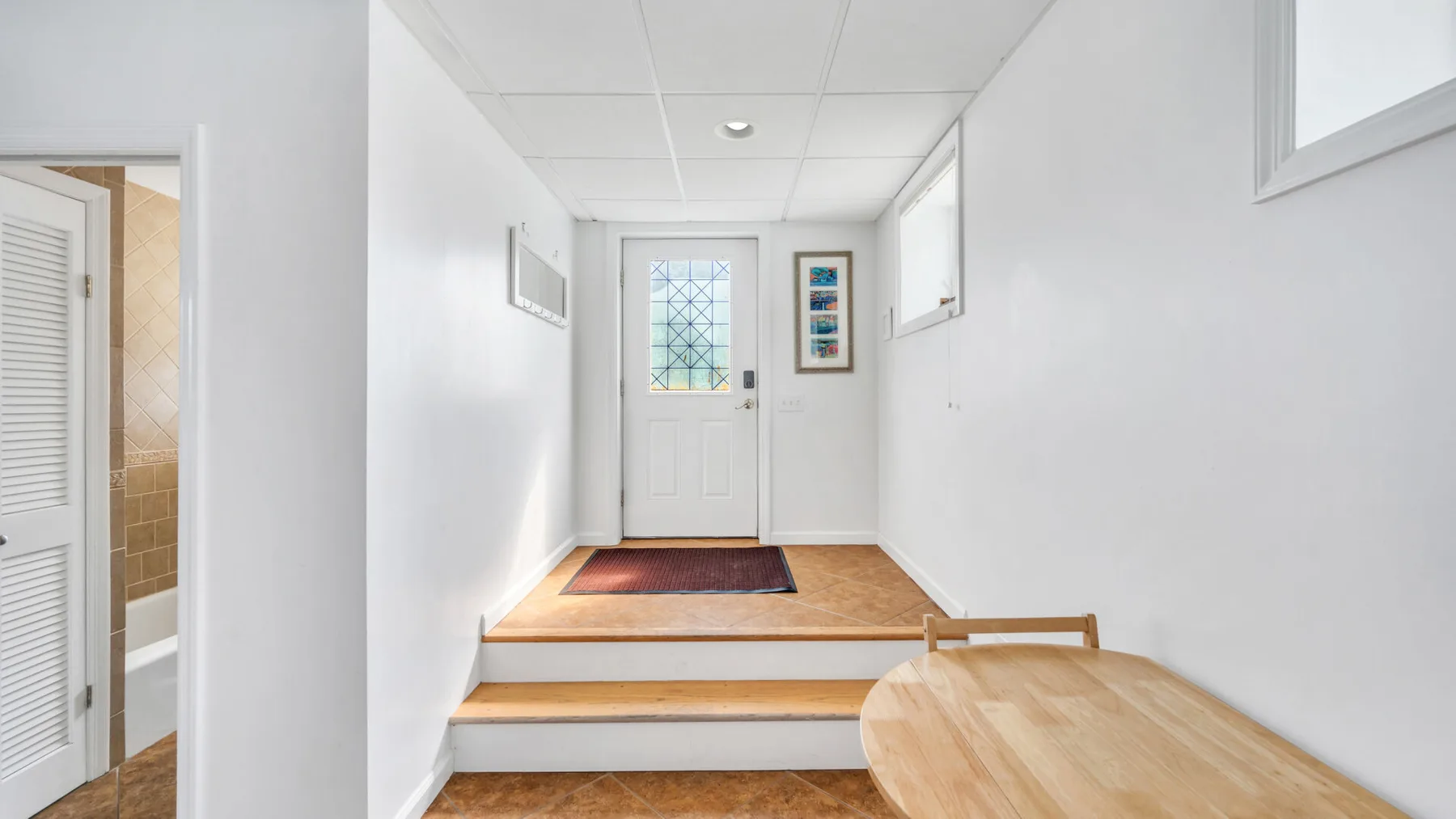 Un recibidor luminoso con una puerta de entrada y una pequeña mesa de madera.