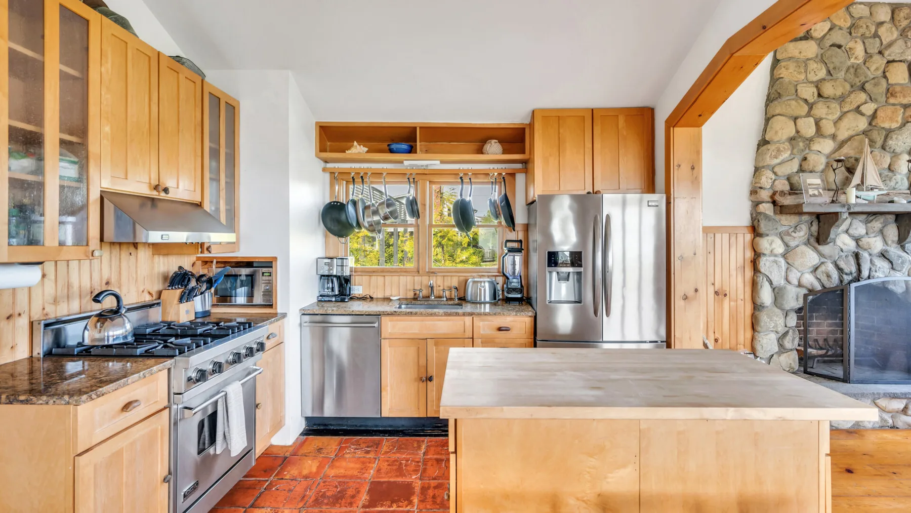 Una cocina luminosa con gabinetes de madera, electrodomésticos de acero inoxidable y una isla central.