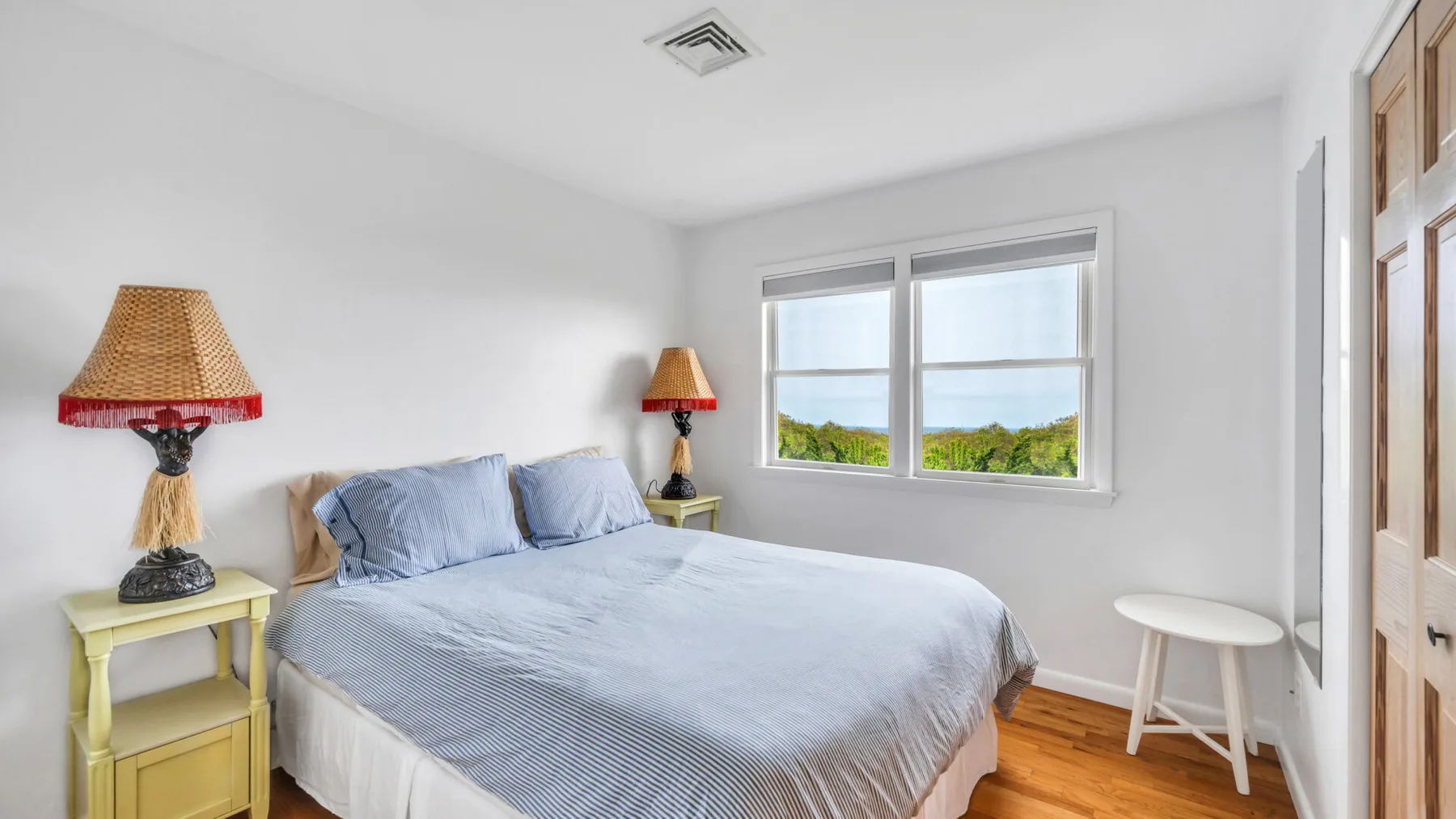 Un dormitorio luminoso con una cama, mesitas de noche y una ventana con vistas a la vegetación.
