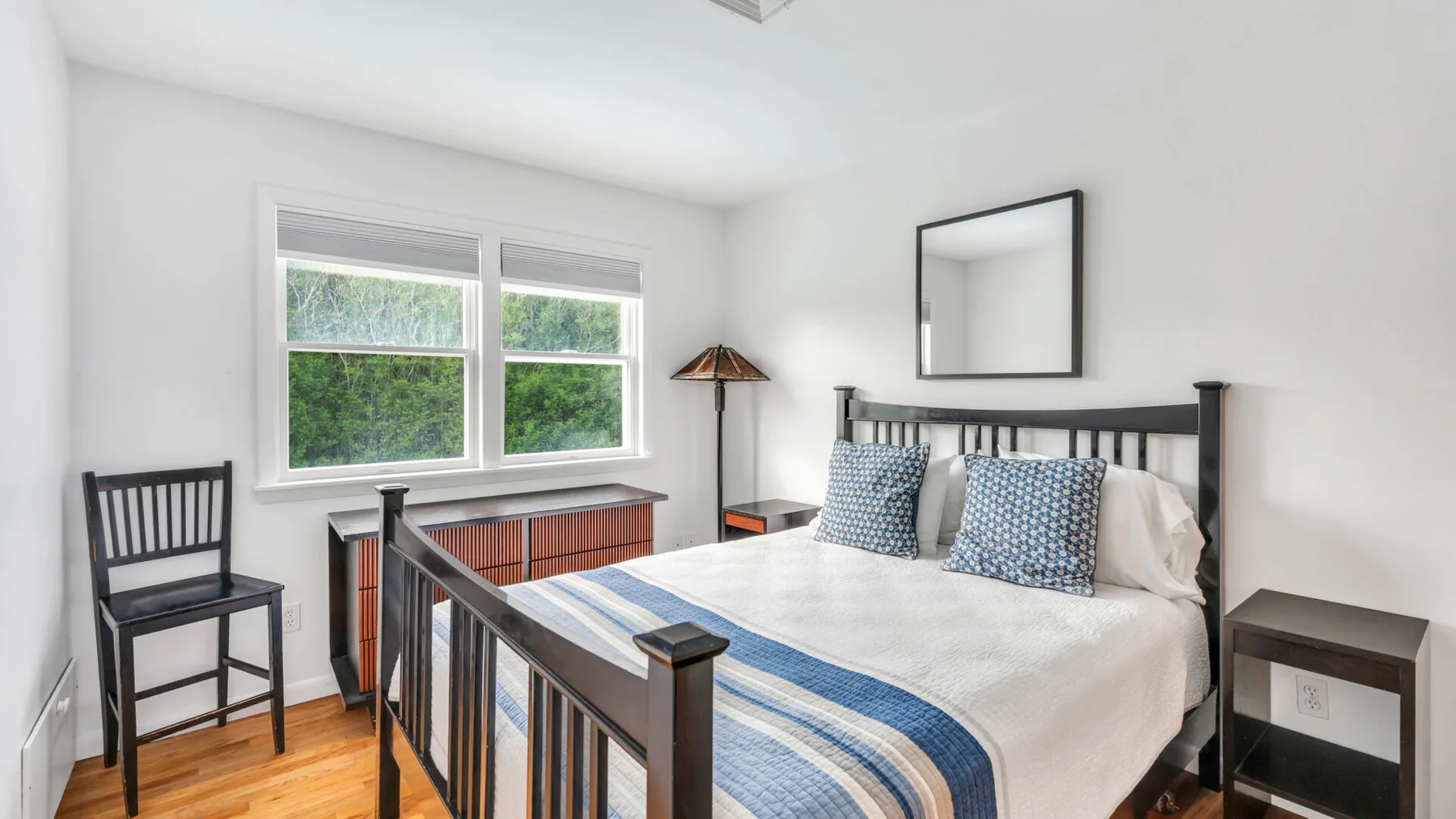 Un dormitorio con una cama, dos ventanas y suelo de madera.