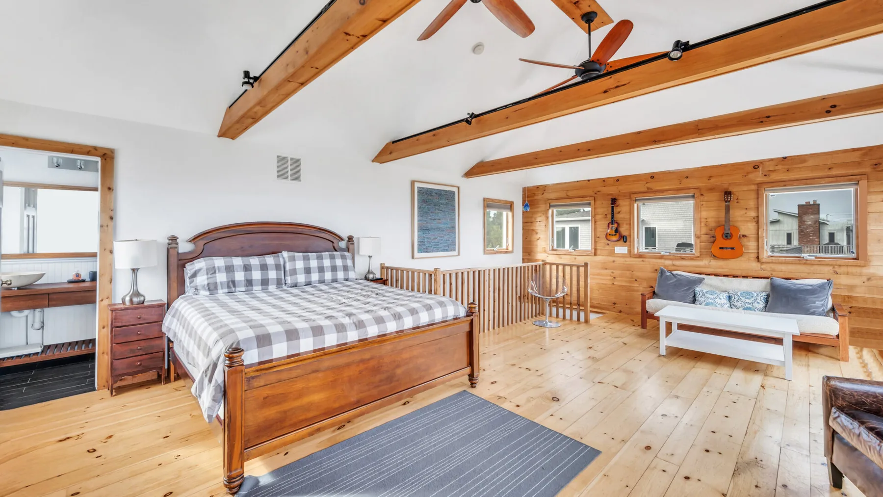 Un dormitorio con una cama de madera y una zona de estar junto a la pared revestida de madera.