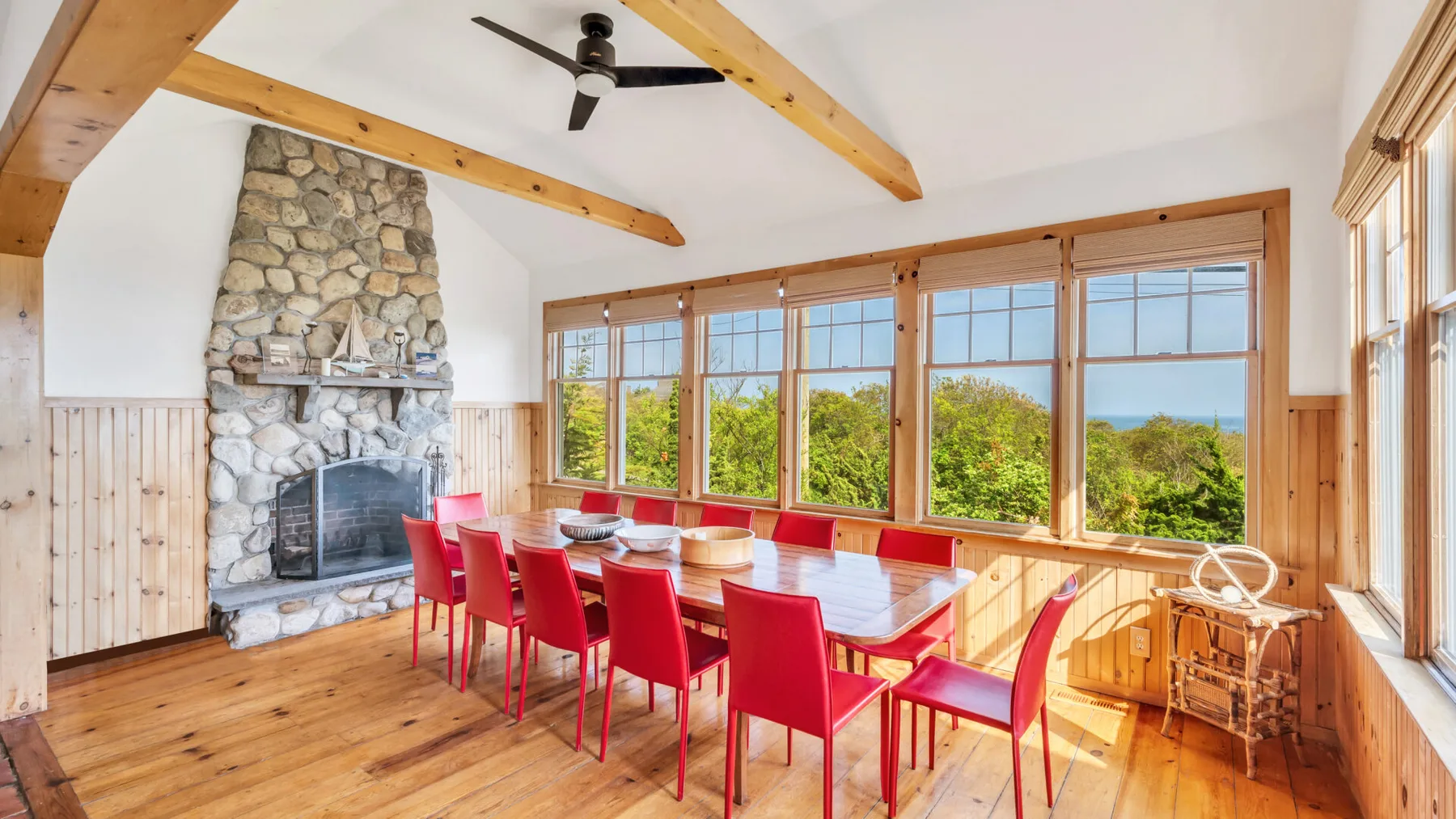 Un comedor con una mesa larga y asientos rojos junto a grandes ventanas.