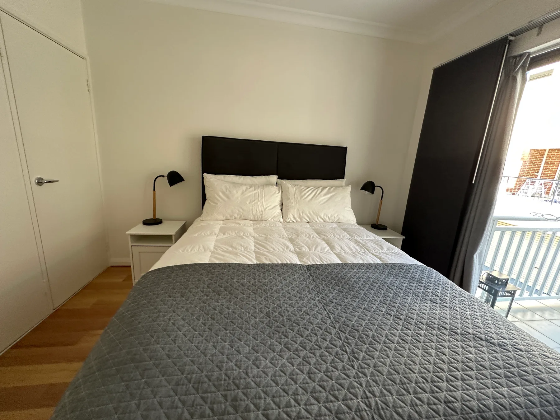 Un dormitorio con una cama, mesitas de noche y una puerta al balcón.