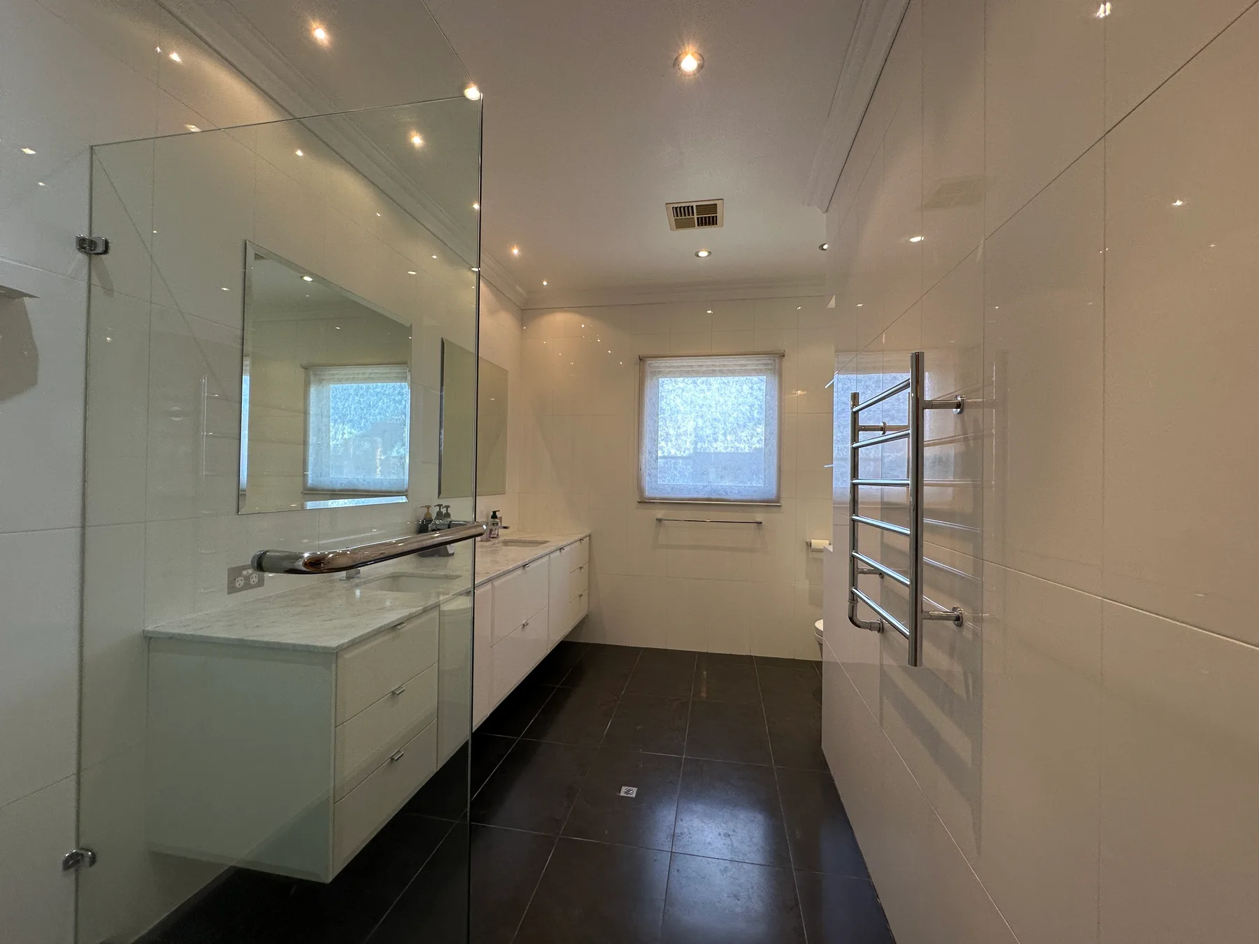 Un baño luminoso con azulejos, un lavabo largo, espejo y ventana.