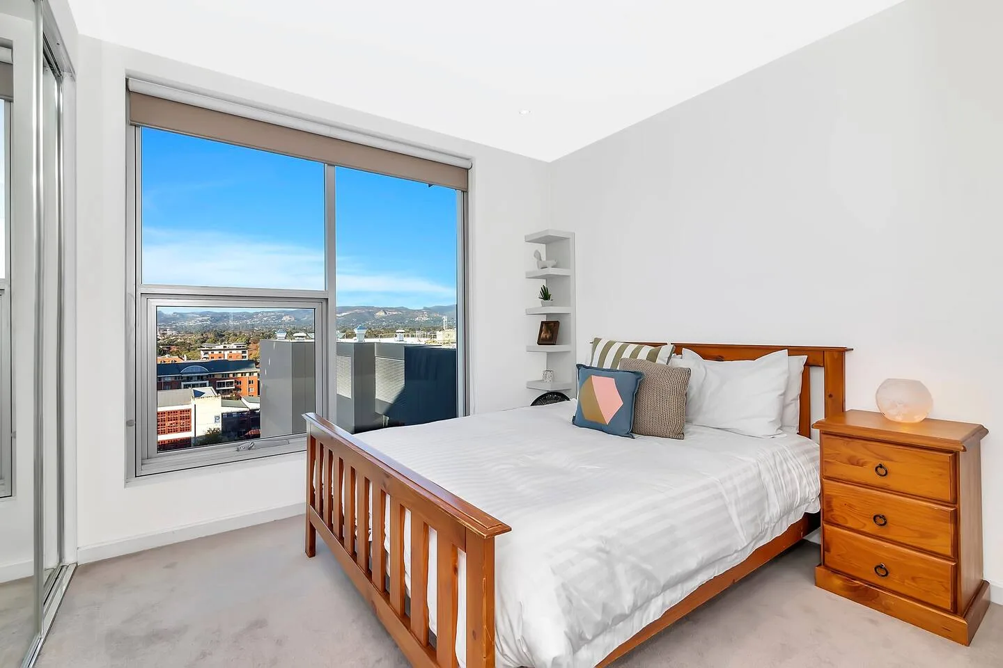 A bedroom with a bed and a large window overlooking the city.