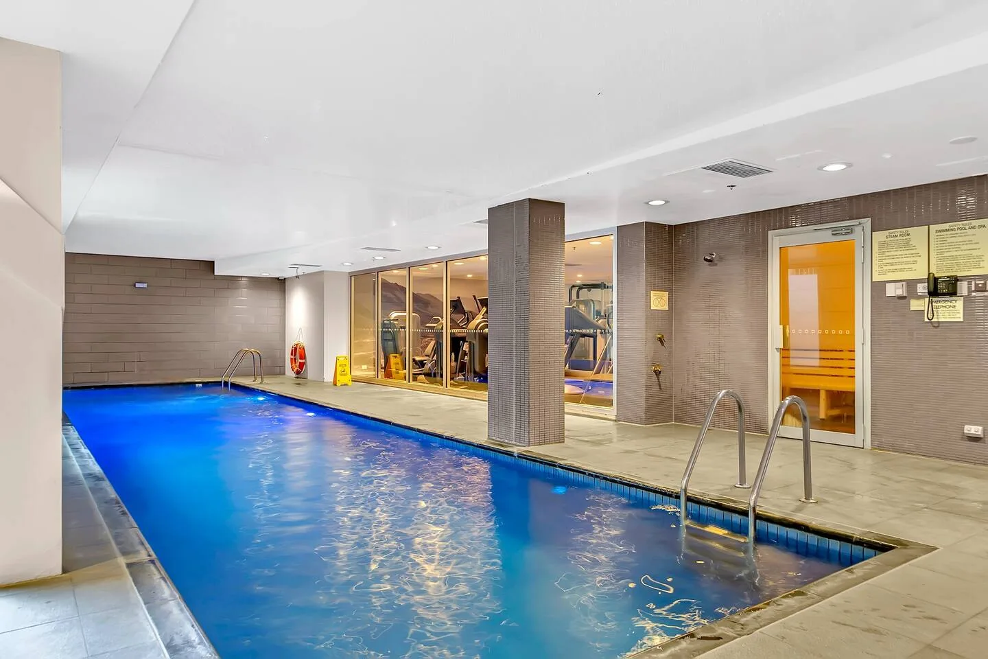 An indoor swimming pool with a metal ladder beside a tiled wall.