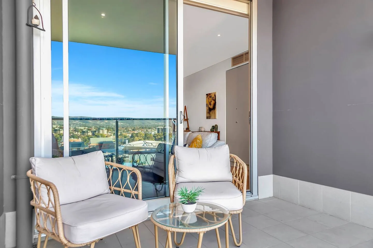 A balcony seating area overlooks a distant city beneath a clear blue sky.