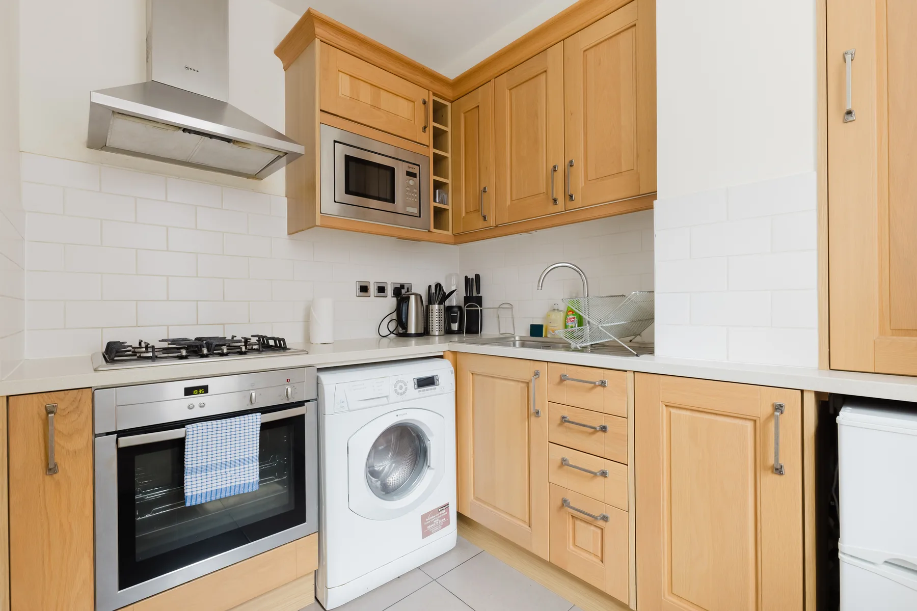 Una cocina compacta con armarios de madera, una estufa y una lavadora.