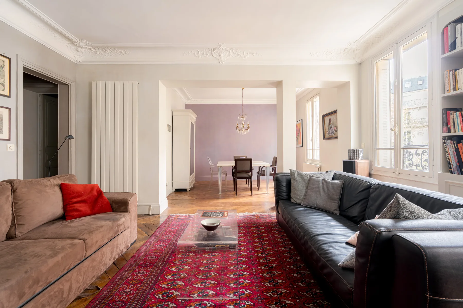 A bright living room with seating around a patterned rug and a dining area beyond.