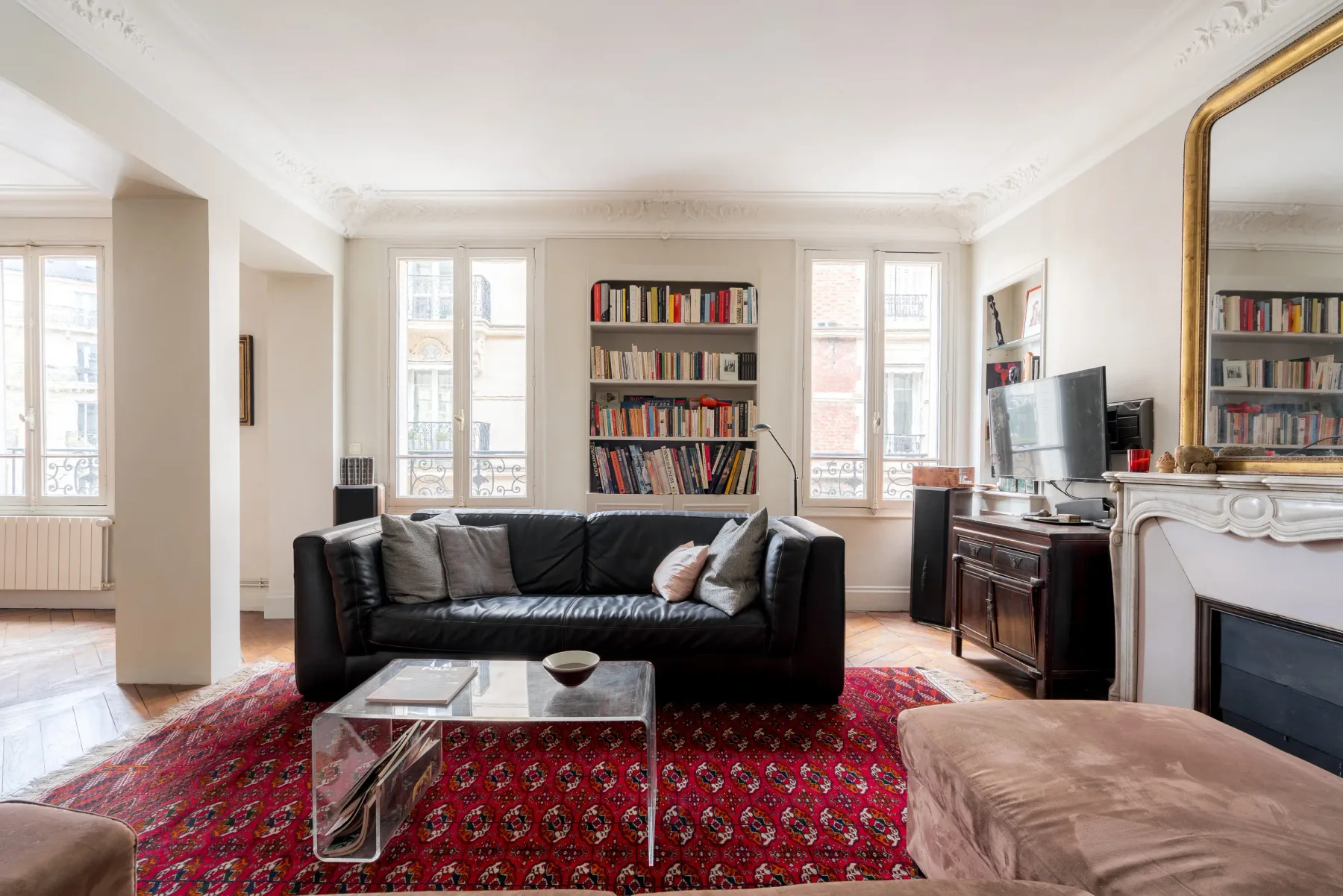 A bright living room with a black sofa, bookshelves, and large windows.