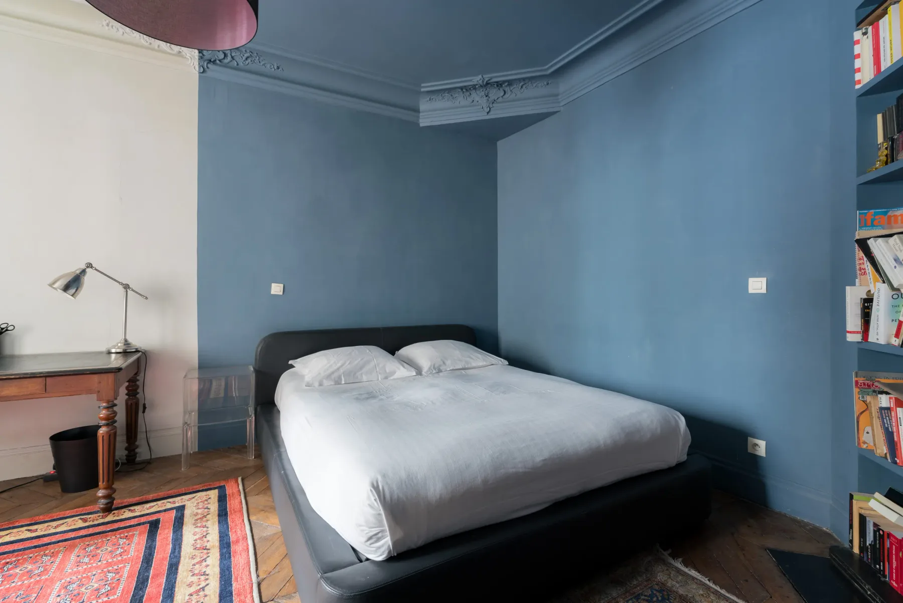 A bedroom with a bed against blue walls and a colorful rug.