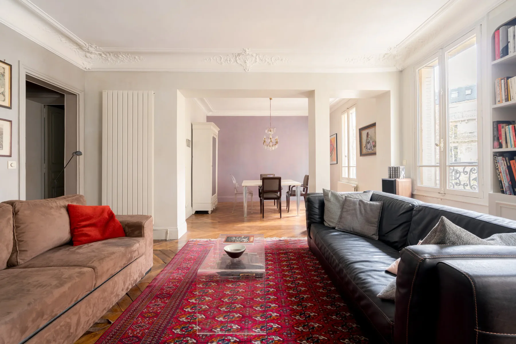 A bright living room with seating around a red patterned rug.