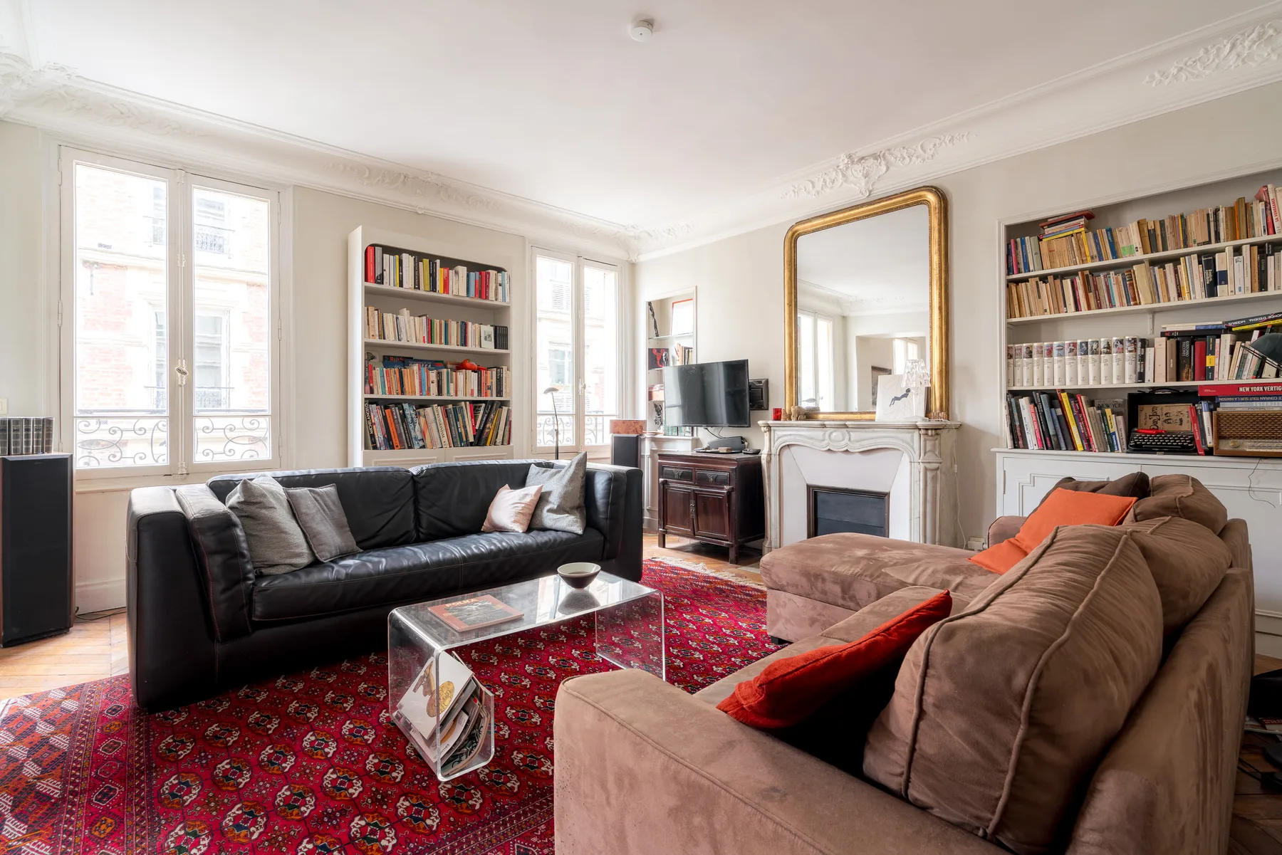 A living room with sofas, bookshelves, and a red patterned rug.
